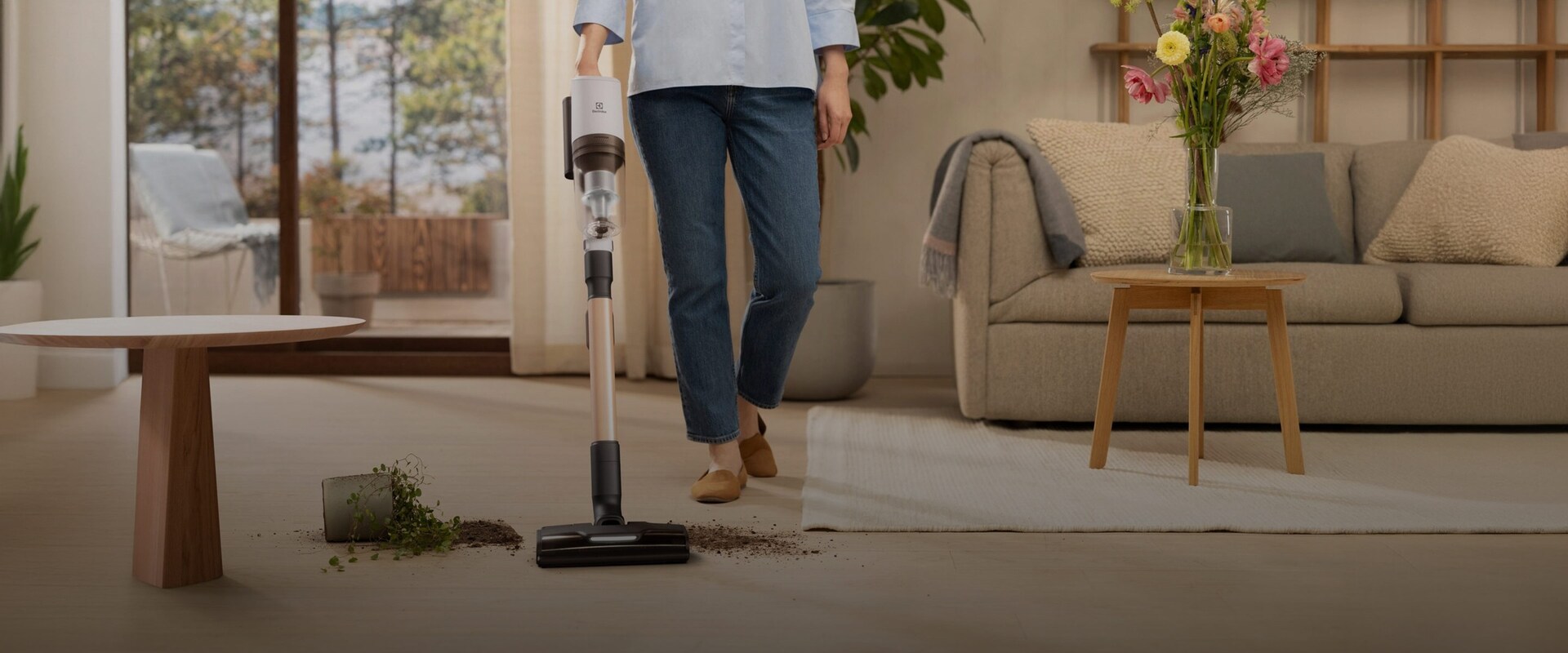 En kvinna använder en Electrolux skaftdammsugare för att städa upp jordspill.